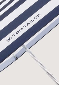 Parasol de plage rayé bleu et blanc avec une structure en métal, portant la marque "TOM TAILOR" imprimée sur le tissu, au toucher lisse.