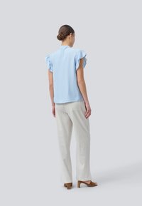 Light blue blouse with flutter sleeves, paired with cream and beige striped wide-leg pants. Wood-heeled sandals complete the look.