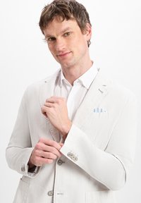 Light gray blazer with a textured fabric, two buttons, and a pocket square featuring blue stripes. Worn over a white shirt.