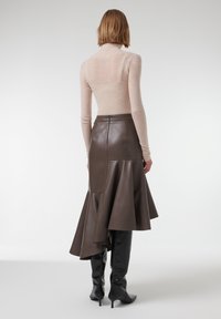 Jupe en cuir marron avec un ourlet évasé, associée à un col roulé ajusté beige clair. Des bottes noires à talons hauts jusqu'aux genoux complètent le look.