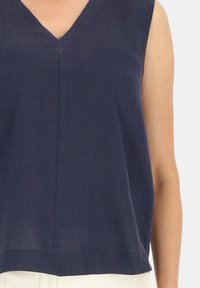 Granatowa lniana bluzka bez rękawów z dekoltem w kształcie litery V, prostym dołem i lekko luźnym krojem, z widocznymi detalami przeszycia.