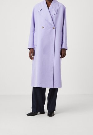 Personne portant un long manteau lavande avec de larges revers, des boutons croisés, un pantalon noir et des chaussures noires pointues.