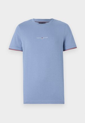 Hellblaues Baumwoll-T-Shirt mit Rundhalsausschnitt, das ein kleines weißes Logo und rote Akzentnähte an den Ärmeln für Details aufweist.