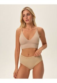 Nude ribbed braletka z regulowanymi ramiączkami oraz dopasowaną wysoką bielizną z tekstem "KOCHAJ SWOJĄ DUSZĘ" na pasku. Gładka tekstura.