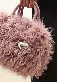 Lyserød faux fur håndtaske med fluffy tekstur, sølv hjerteaccent og læderstropper. Har en stor, rund form og blødt, krøllet materiale.