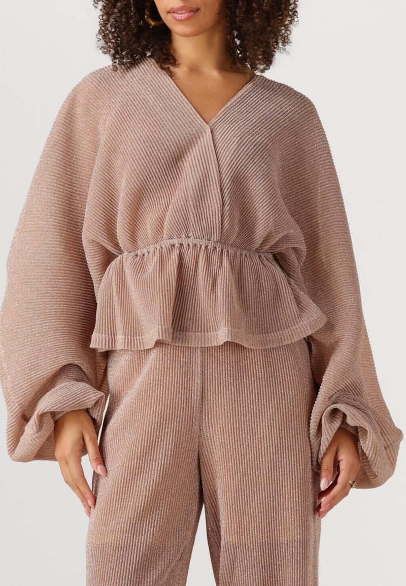 Perzikbruin, geribbeld topje met een V-hals, elastische taille en brede mouwen. De stof heeft een subtiele glans en een vloeiende structuur.