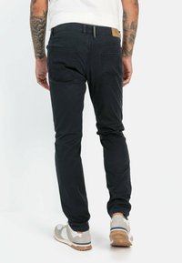 Slim-fit black jeans with stitched back pockets, a visible waistband label, and tapered legs. Material appears soft with a subtle texture.