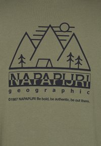 T-shirt vert olive avec un graphique de montagne noire, des arbres et du texte. Texture lisse avec un col rond.
