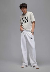 Jasnoszara koszulka z odważnym czarnym nadrukiem "23", w połączeniu z białymi dresami z czarnym logo Jordana. Białe sneakersy z szarymi akcentami.