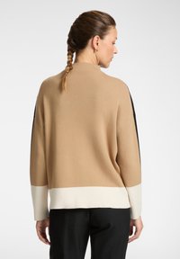 Maglione a maniche lunghe in beige, nero e crema. Texture a coste con un fit rilassato, presenta un design a blocchi di colore e un collo alto.