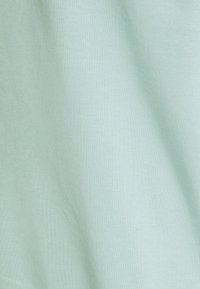 Light green cotton fabric with a soft texture, showcasing a smooth surface and even, subtle knit pattern. No notable accents or hardware.