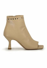 Stivale alla caviglia in pelle beige con punta aperta, dotato di una linea decorativa di borchie metalliche attorno alla parte superiore e un tacco basso e svasato.