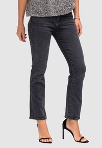 Jeans en denim noir stretch avec une coupe slim et une jambe droite. Associés à des talons aiguilles noirs, mettant en valeur un style décontracté mais ajusté.