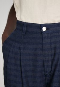 Marine gestreepte broek met een gladde textuur, voorzien van een knoopsluiting en plooiingen, gemaakt van een lichtgewicht stof.