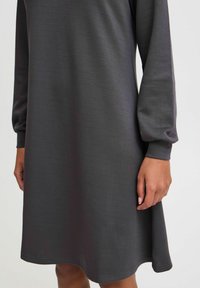Graues langärmliges Kleid aus weichem Stoff, mit lässiger Silhouette, rundem Ausschnitt und subtiler Saumlinie mit leichtem Ausschlag.