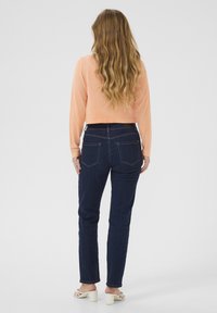 Virkat stickat kort peachtröja, framfickor, marinblå jeans, rak passform, tre bakfickor, slät textur och konturerad sömnad.