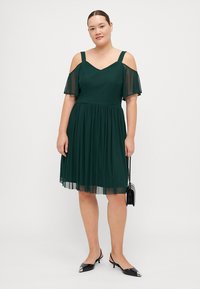 Vestito verde con maniche a spalle scoperte, corpino aderente e gonna plissettata. Realizzato in tessuto leggero, presenta una scollatura a V e una texture fluida.