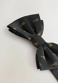 Black bow tie made of woven fabric, featuring a repeating gold pattern of small crowns. Bow structure with a smooth texture.