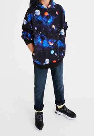 Sweat à capuche noir avec imprimé galaxie et planètes, assorti à un jean en denim retroussé et des baskets noires à semelles blanches.