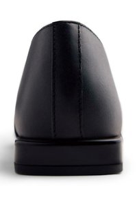 Chaussure en cuir noir avec une texture lisse, un bout arrondi, des coutures subtiles et une semelle noire basse avec un léger talon.