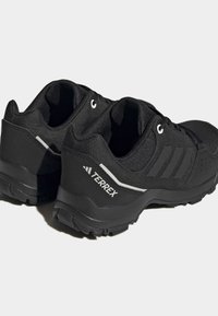 Czarne buty sportowe z teksturowanej sintetycznej cholewce, wyściełanym kołnierzem, trzema białymi paskami po boku i solidną gumową podeszwą.