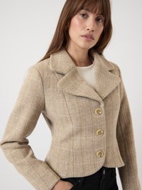 Beige Jacke im Hahnent pattern mit Reverskragen, vier großen Knöpfen, taillierter Passform und strukturiertem Stoff.