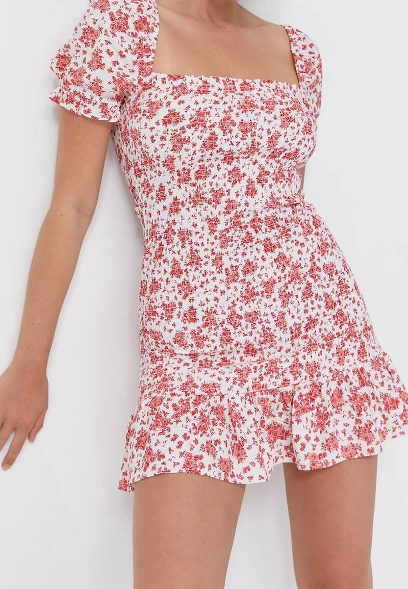 Robe à motif floral avec une base blanche et des fleurs rouges, dotée d'un col carré, de manches courtes bouffantes et d'un ourlet volanté.