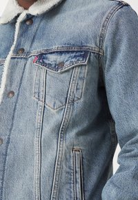 Veste en denim bleu clair avec col en shearling blanc, boutons en métal, poche à rabat poitrine avec bouton et poche passepoilée latérale.