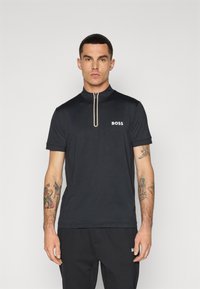 Kort zip-up, svart polo shirt med krage, som har den vita "BOSS"-logotypen på vänster bröst och en texturerad tyg.