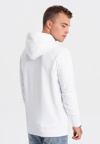 Witte hoodie met een trekkoord, ribgebreide manchetten en een kangoeroezak. Zachte textuur, comfortabele pasvorm en zichtbare stikseldetails.