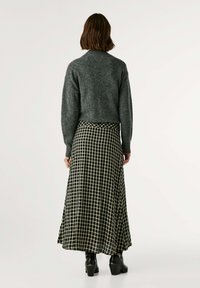 Maglione grigio lavorato a maglia con colletto alto, abbinato a una gonna a scacchi bianco e nera che arriva fino al pavimento. Stivali neri con tacco completano l'outfit.