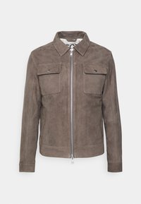 Ruskea mokkajakku, jossa on klassinen kaulus, etuvetoketju ja kaksi rintataskua läpillä. Sujuva pintakuvio ja muotonsa pitävä istuvuus.