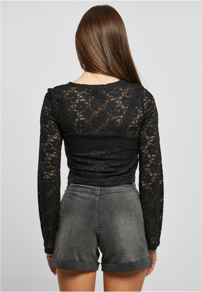 Svart blonde langermet topp med blomstermønster, kombinert med grå denimshorts med rullekant. Vist bakfra.