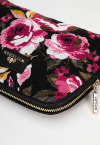 Clutch met bloemenpatroon van zwarte stof, versierd met roze en witte rozen. Gouden ritsaccent en zichtbaar genaaid merklabel.