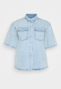 Lys blå denimskjorte med korte ermer, som har to frontlommer og er dekorert med små sølvnitter over hele.