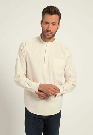 Helle beigefarbene Langarmbluse mit Stehkragen, Knopfleiste und einer Brusttasche. Figurbetonter Schnitt mit minimaler Textur, kombiniert mit dunklen Jeans.