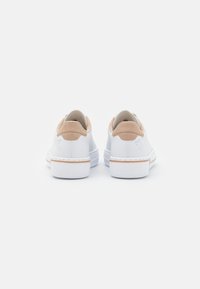 Baskets blanches avec des accents en suède beige au talon, matériau texturé et design minimaliste. Elles disposent d'une semelle en caoutchouc blanche et de détails surpiqués.