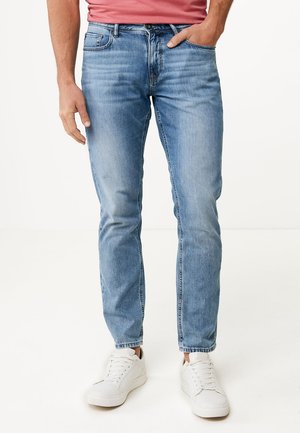 Jeans in denim blu chiaro con taglio dritto, cinque tasche e una finitura scolorita, abbinati a sneakers bianche e una maglietta rossa.