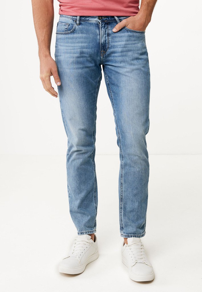 Jeans de mezclilla azul claro con corte recto, cinco bolsillos y un acabado desgastado, combinados con zapatillas blancas y una camiseta roja.