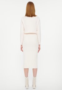 Gebreid tweedelig outfit in licht crème, bestaande uit een cropped trui en een midi rok. Glad textuur, aansluitend ontwerp, gecombineerd met laarzen met rits bij de enkels.