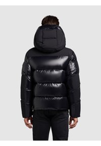 Črna puhasta jakna z sijočim zaključkom, z odlomljivo kapuco, vodoravnimi šivi in sproščenim krojem. Prikazan zadnji pogled.