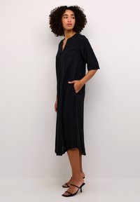 Black midi dress with a V-neck, short sleeves, and side pockets. Lightweight fabric with a smooth texture and slight side slits.