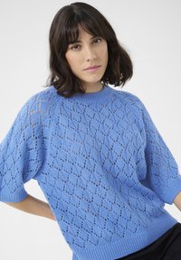 Maglione lavorato a maglia azzurro chiaro con un motivo a rombi, maniche corte e colletto e orli a coste. La texture è leggera e ariosa.