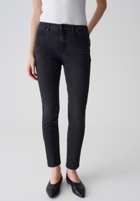Jean slim noir avec une texture lisse, design à cinq poches et légère élasticité pour le confort. Portés avec des ballerines noires à bout pointu.