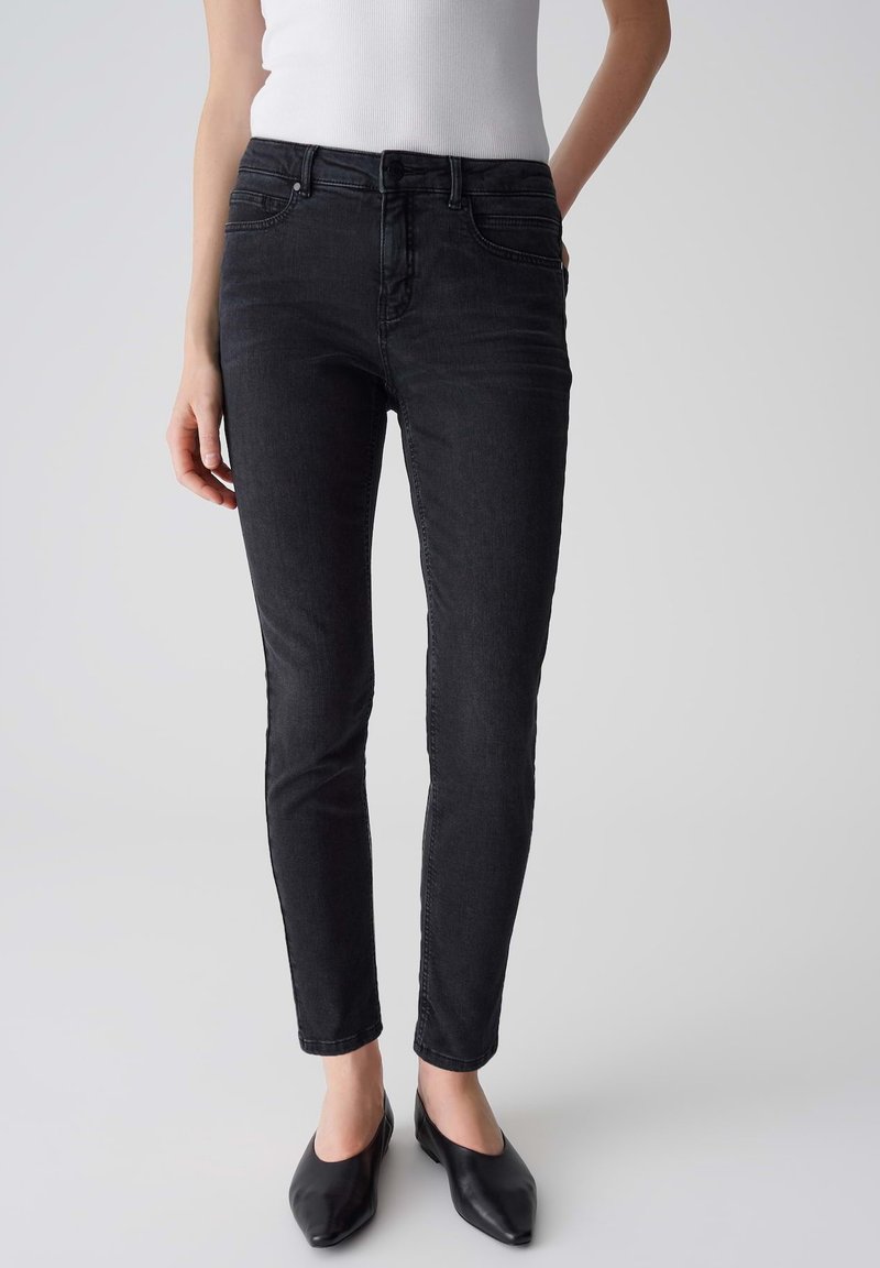 Jean slim noir avec une texture lisse, design à cinq poches et légère élasticité pour le confort. Portés avec des ballerines noires à bout pointu.