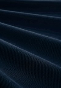 Marineblauer Textilstoff mit ausgeprägter vertikaler Rippung, dessen glatte, weiche Oberflächen subtile Lichtreflexionen über die Falten erzeugen.