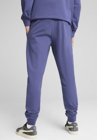 Purple sweatpants with an elastic waistband and cuffs. Material appears soft; features side pockets and a smooth texture.