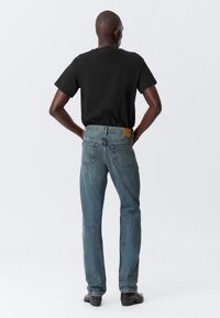 Black cotton t-shirt paired with blue denim jeans. The jeans feature back pockets and a brown leather patch at the waistband.