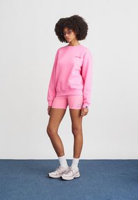 Ružová mikina a zodpovedajúce šortky vyrobené z mäkkej látky. Mikina má malé logo; šortky majú kontrastný lem.