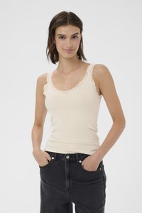 Top a canotta beige chiaro con una texture a coste, bordi in pizzo ondulato sui spallacci e sul collo, abbinato a jeans neri a vita alta.